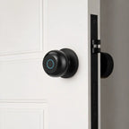 A matte black smart door lock with a circular touch panel and glowing blue ring, mounted on a white paneled door next to a black latch.