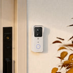 A white smart video doorbell with a black camera lens area and a blue-lit circular button, mounted on a textured beige wall next to a black smart door lock.