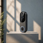 A modern black smart video doorbell with a circular light ring stands on a concrete pedestal against a textured gray wall with soft window shadows.