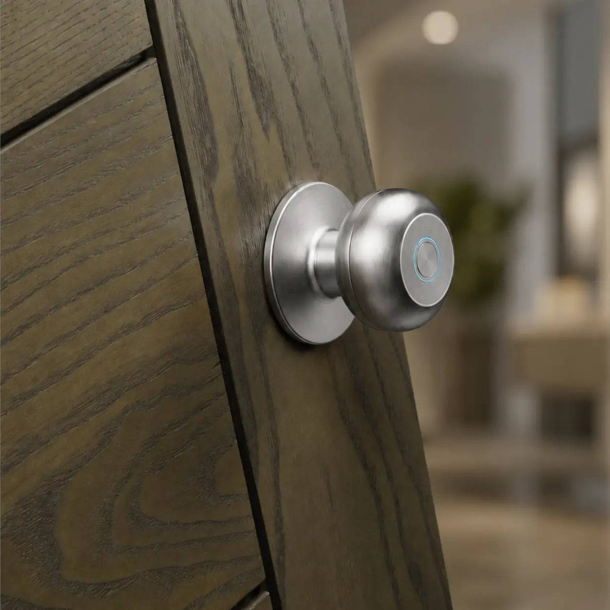 A close-up of a brushed silver smart door knob mounted on a dark wood door, with a softly blurred modern interior in the background.